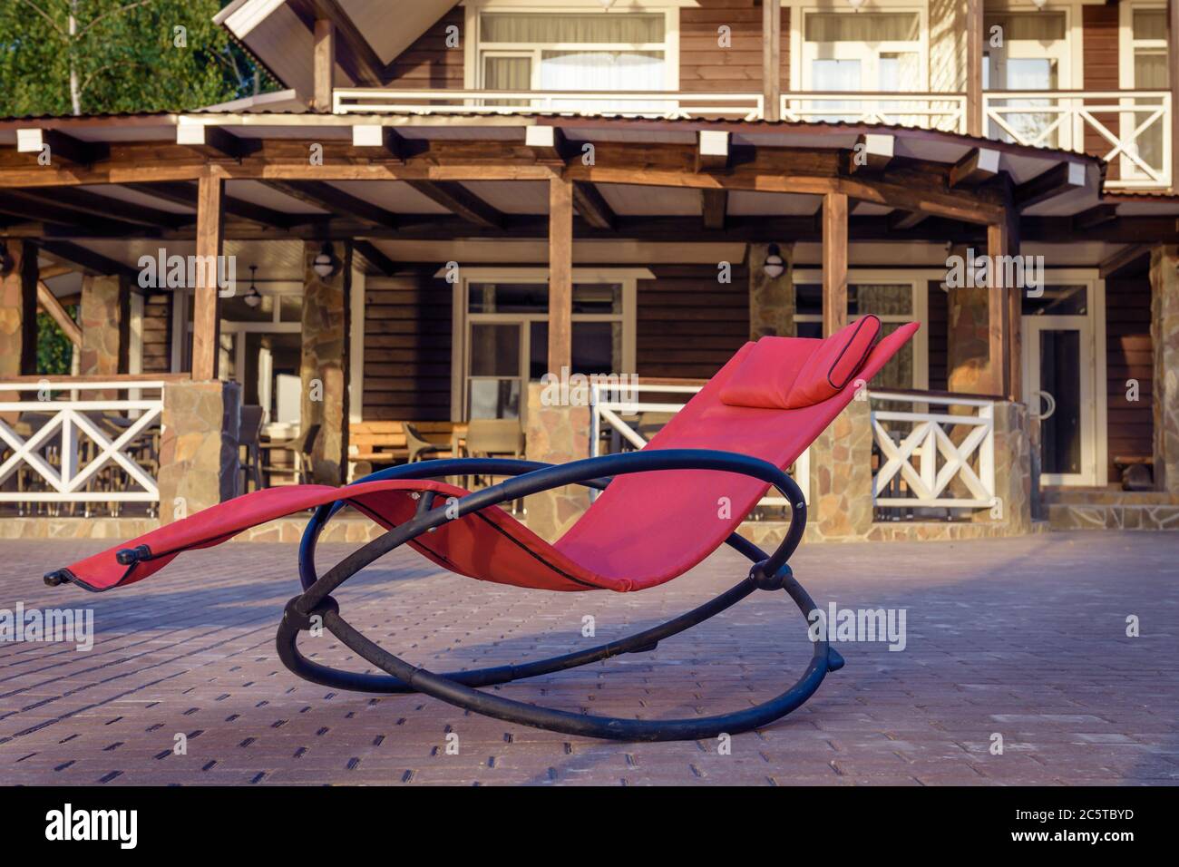 Red chair rocking chair for relaxation, close-up, against the background of a wooden house. Stock Photo