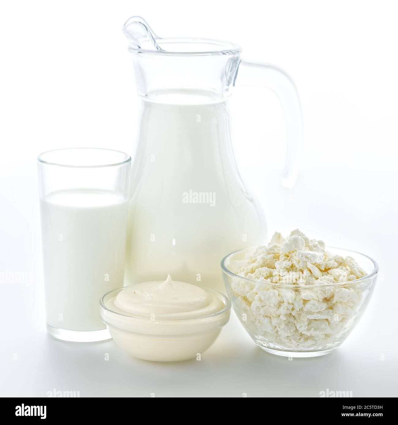 A transparent glass and a jug of useful fresh milk along with a plate of cottage cheese on a clean white background. Dairy kitchen is very useful for Stock Photo