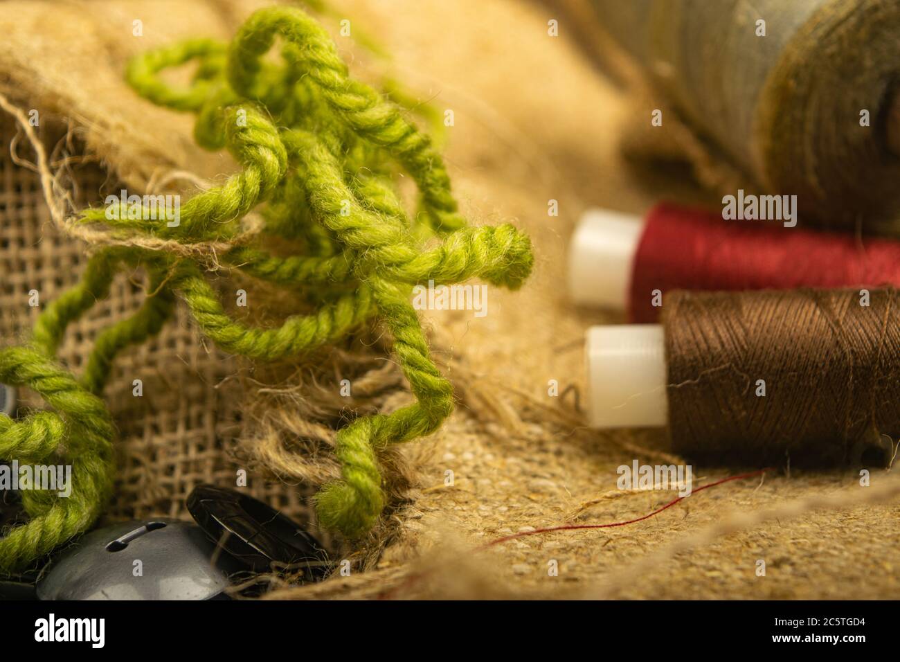 Various buttons and multicolored threads on coarse-textured burlap. Close up Stock Photo