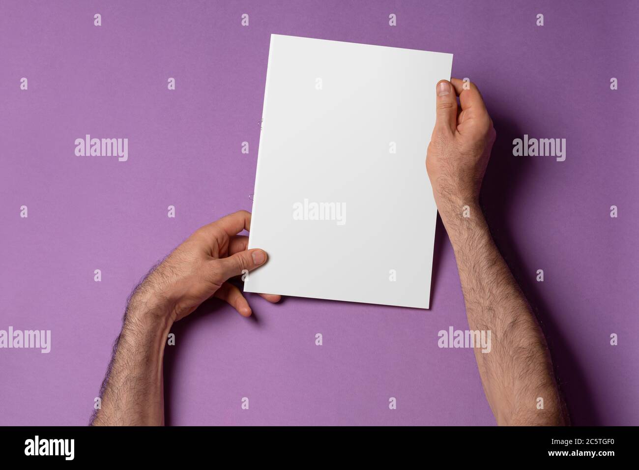 Male hands holding a catalog with blank cover on purple background