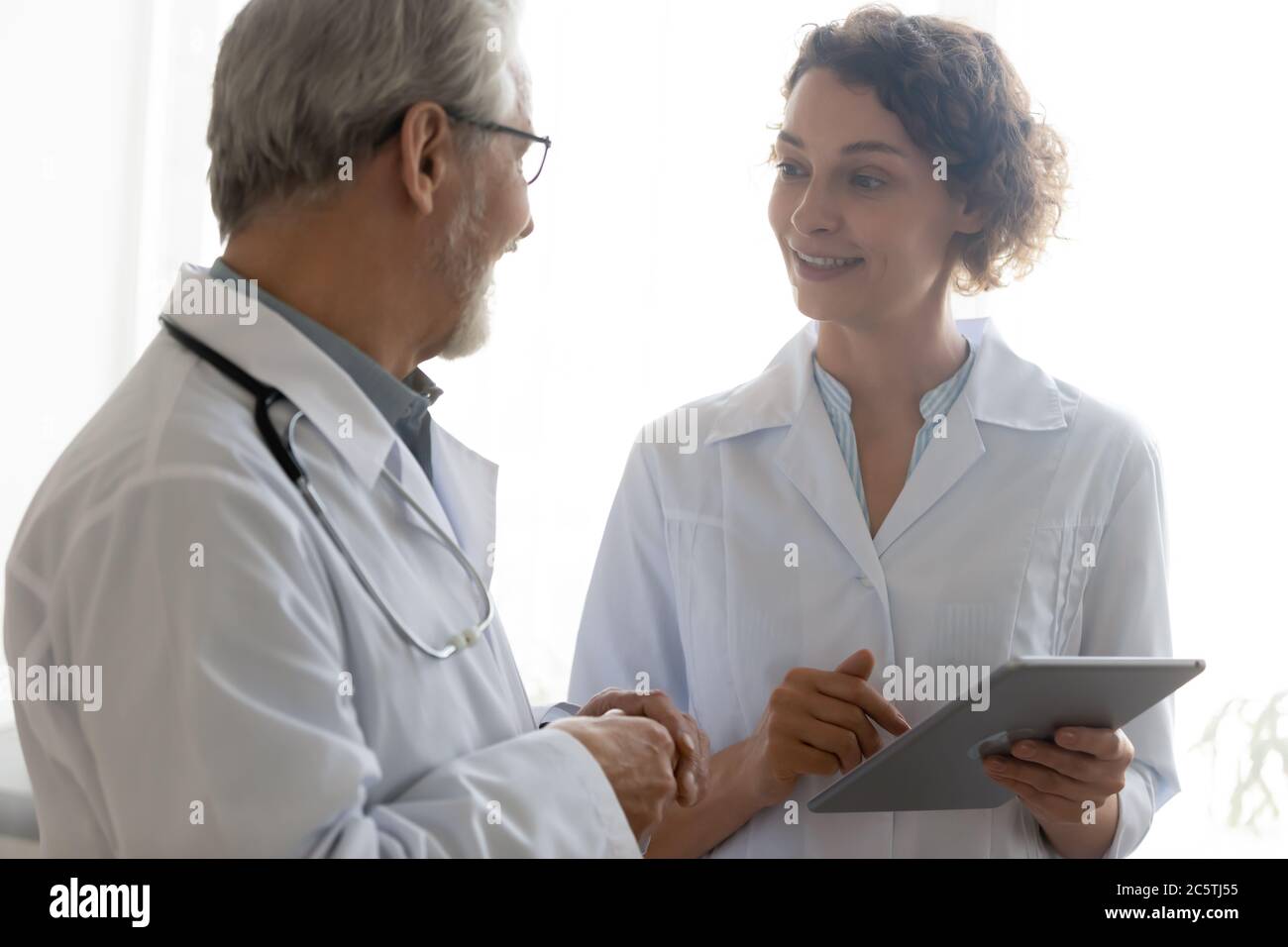 Smiling diverse doctors talk discuss issue using tablet Stock Photo