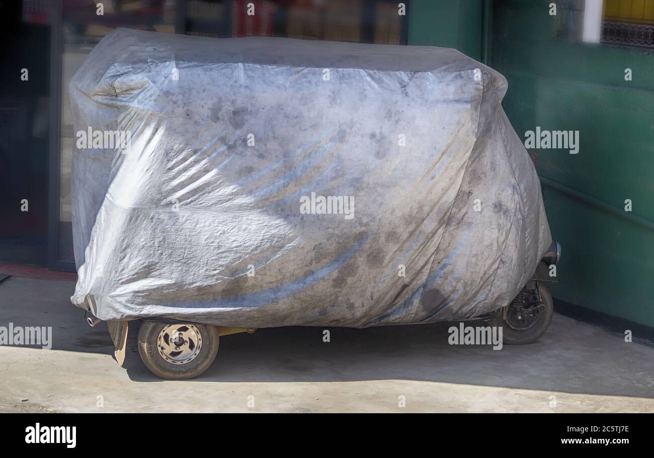Tuk tuk is covered with an old tent for storage. Storing motorcycle under  protective cover. Hidden unknown mystery motorcycle Stock Photo - Alamy