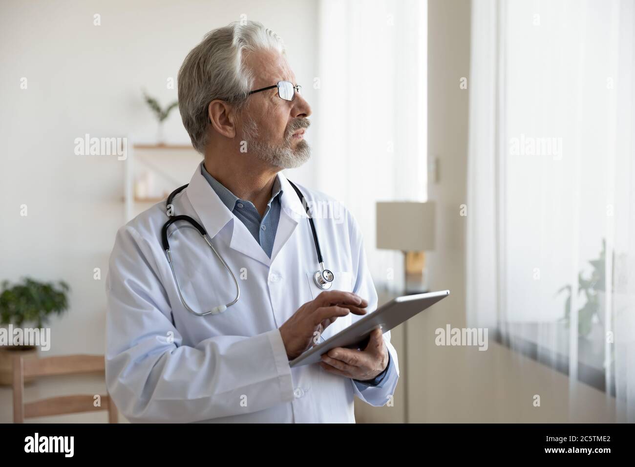 Pensive senior doctor use tablet making decision Stock Photo