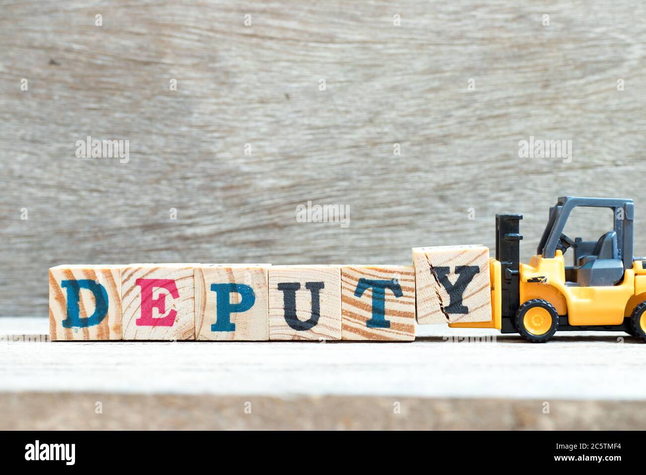 Toy forklift hold letter block y to complete word deputy on wood background Stock Photo