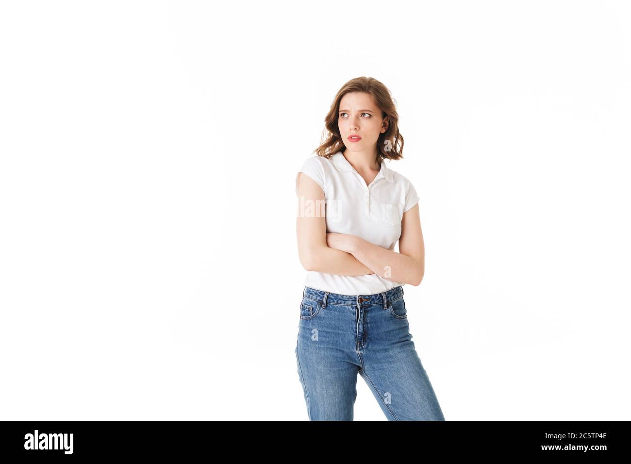 Portrait of young upset lady standing in t shirt and jeans and sadly looking aside on white background isolated Stock Photo