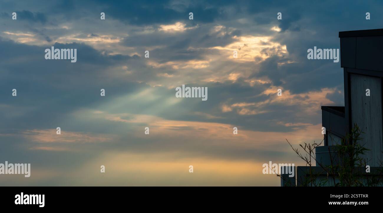 Rays of light piercing through the clouds during sunset with parts of rooftops Stock Photo