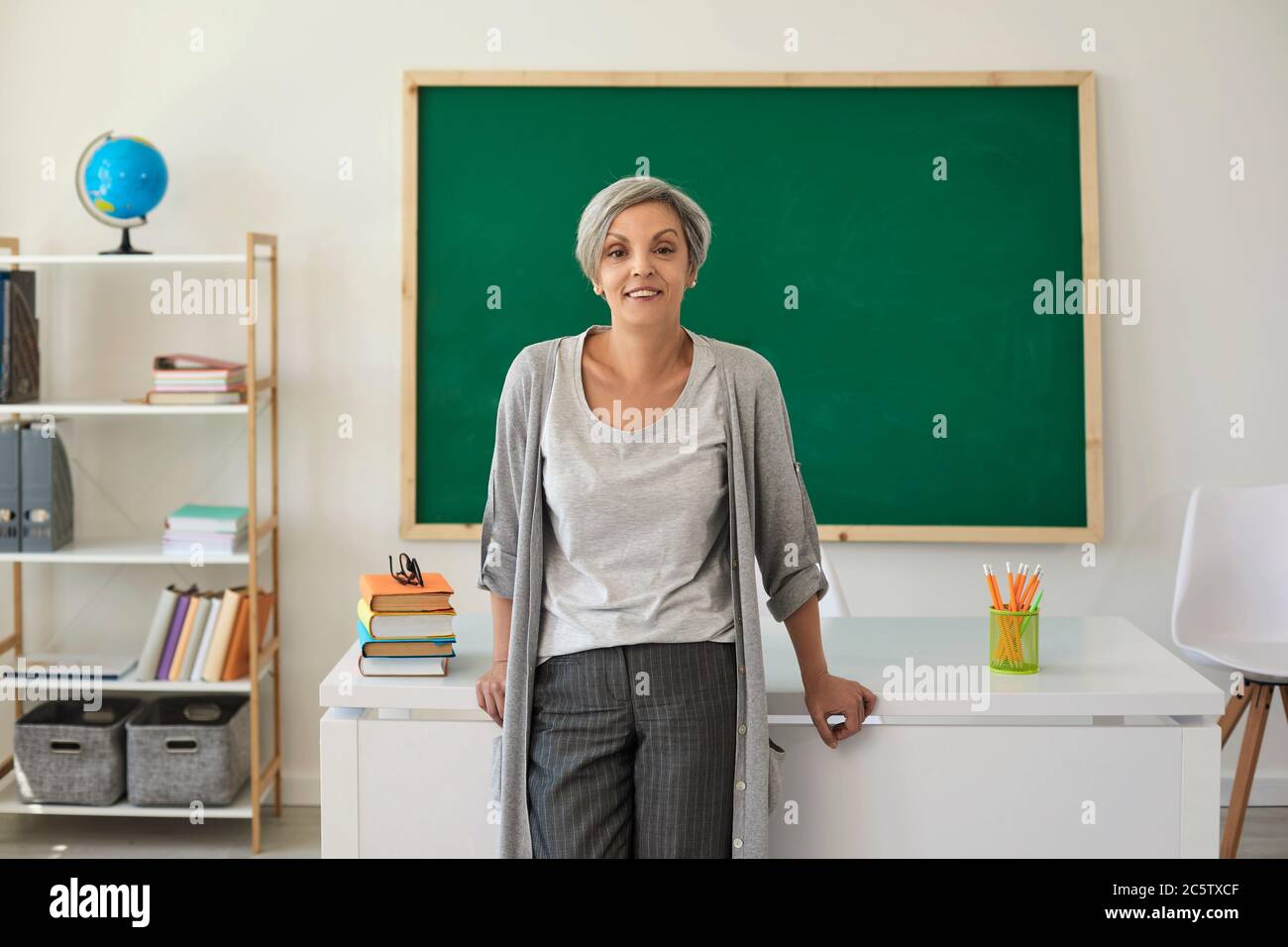 A teacher with gray hair teaches standing in a school class Stock Photo