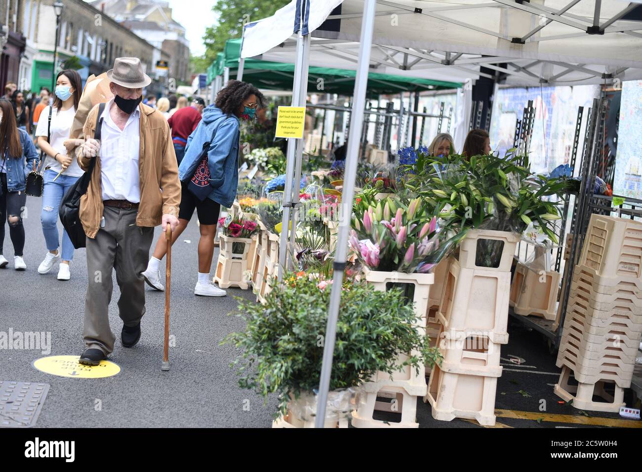 People walk through Columbia Road Flower Market, London, as it reopens following the easing of coronavirus lockdown restrictions across England. Stock Photo