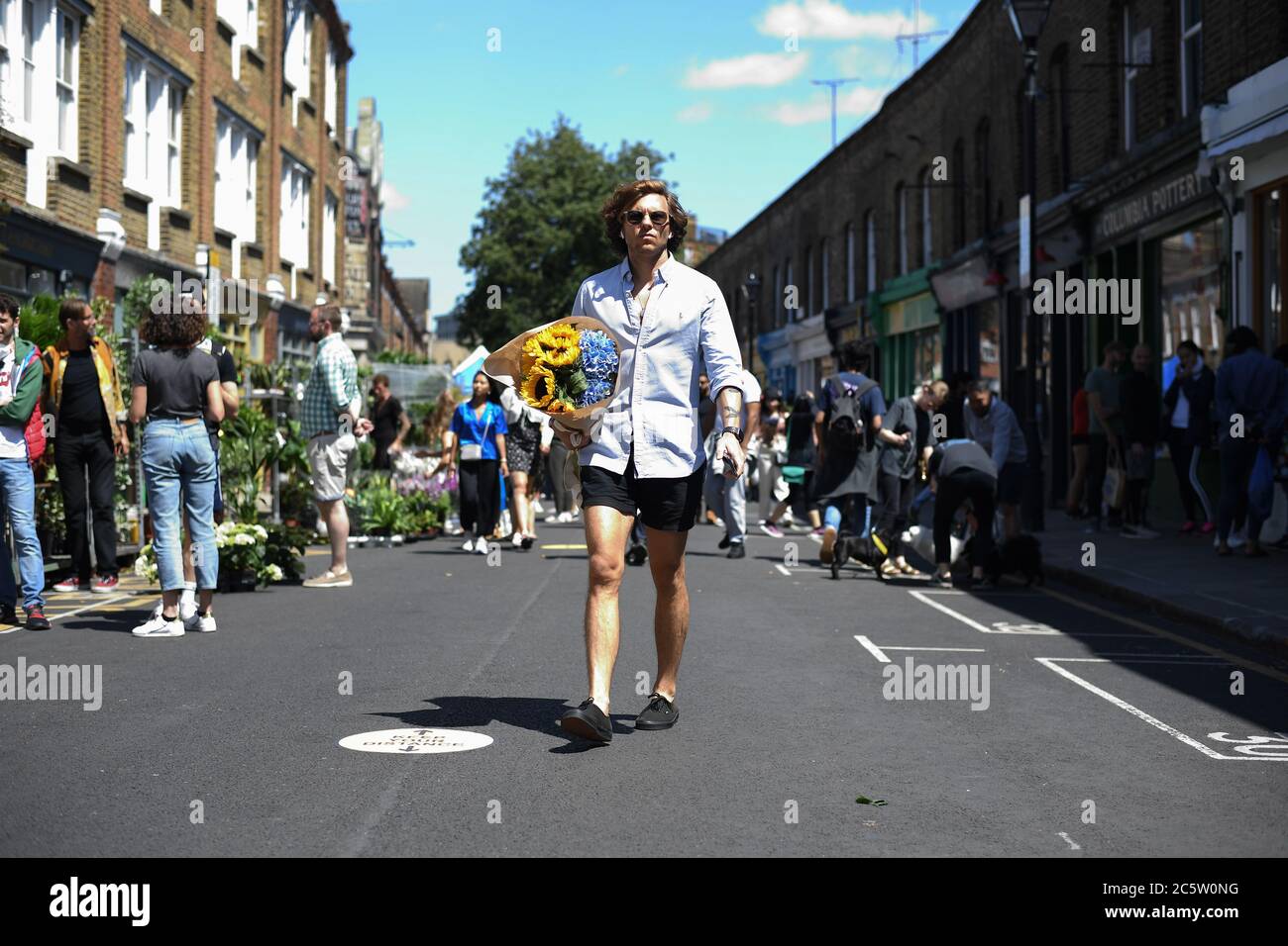 People walk through Columbia Road Flower Market, London, as it reopens following the easing of coronavirus lockdown restrictions across England. Stock Photo