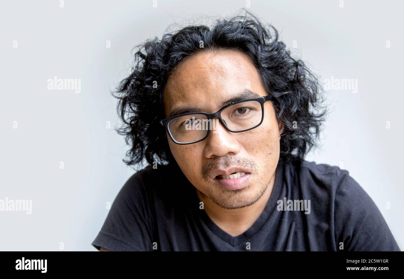 close up angry face and look at camera of asian Thai man with curly hair and glasses in charector of seriously action on white background Stock Photo