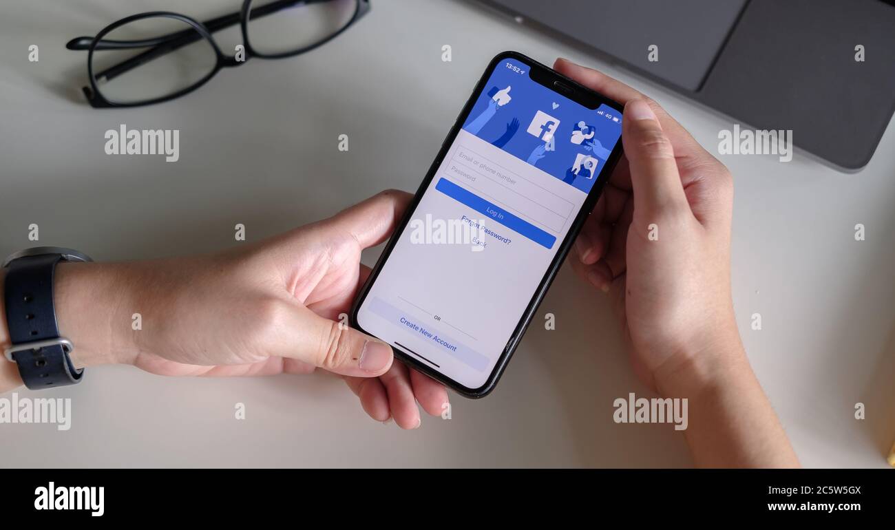 CHIANG MAI ,THAILAND - JULY 3, 2020 : Woman hand holding iPhone X to use facebook with new login screen.Facebook is a largest social network and most Stock Photo