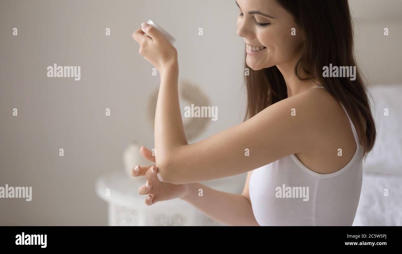 Close up smiling young woman applying moisturizing cream on elbow Stock Photo