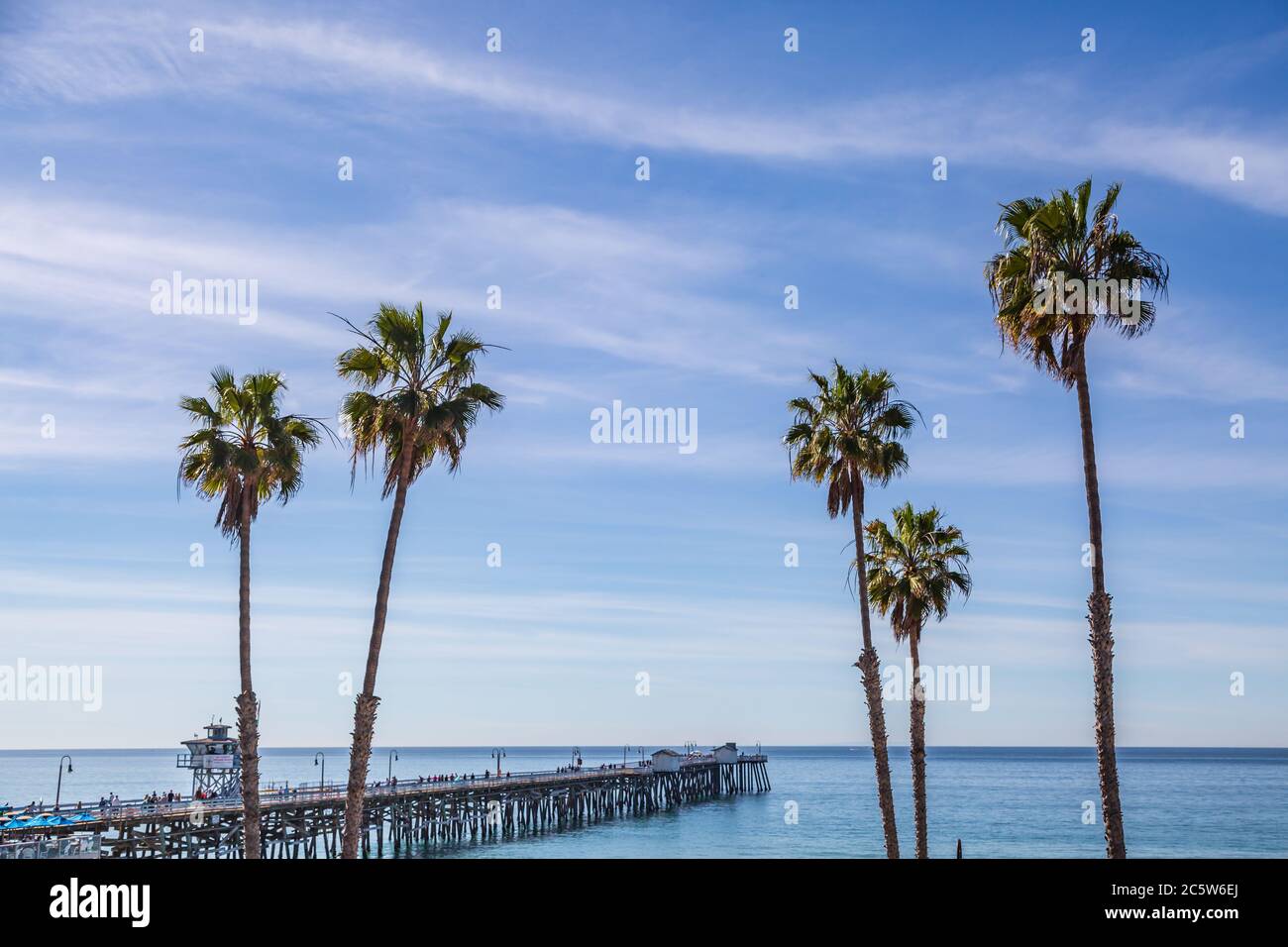 The pier and palm trees at San Clemente beach, with a blue sky overhead Stock Photo