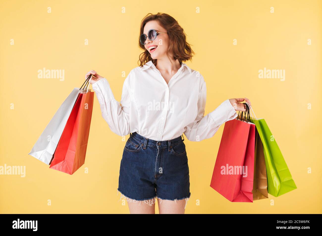 Portrait of beautiful smiling lady in sunglasses standing with colorful shopping bags in hands on over pink background Stock Photo
