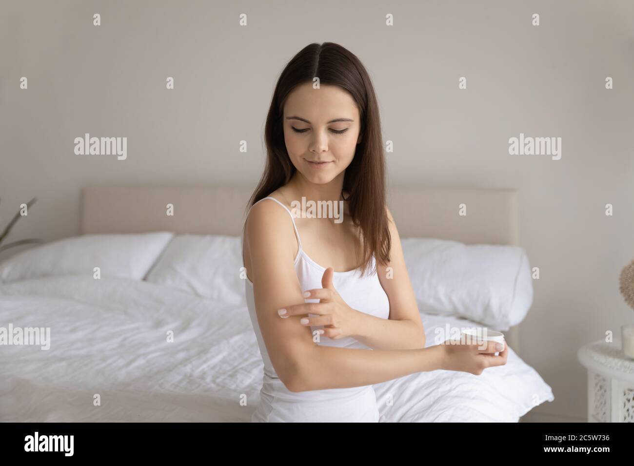 Beautiful satisfied young woman applying moisturizing cream on arm Stock Photo