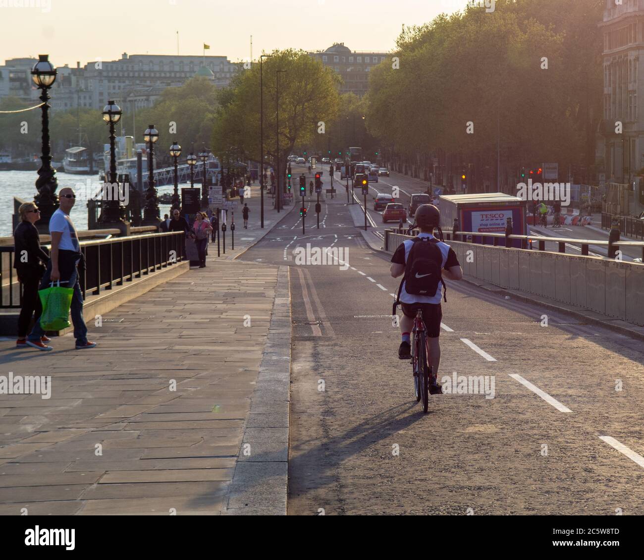 Cyclists, pedestrians and traffic move along the Thames Embankment on a sunny evening in London. Stock Photo