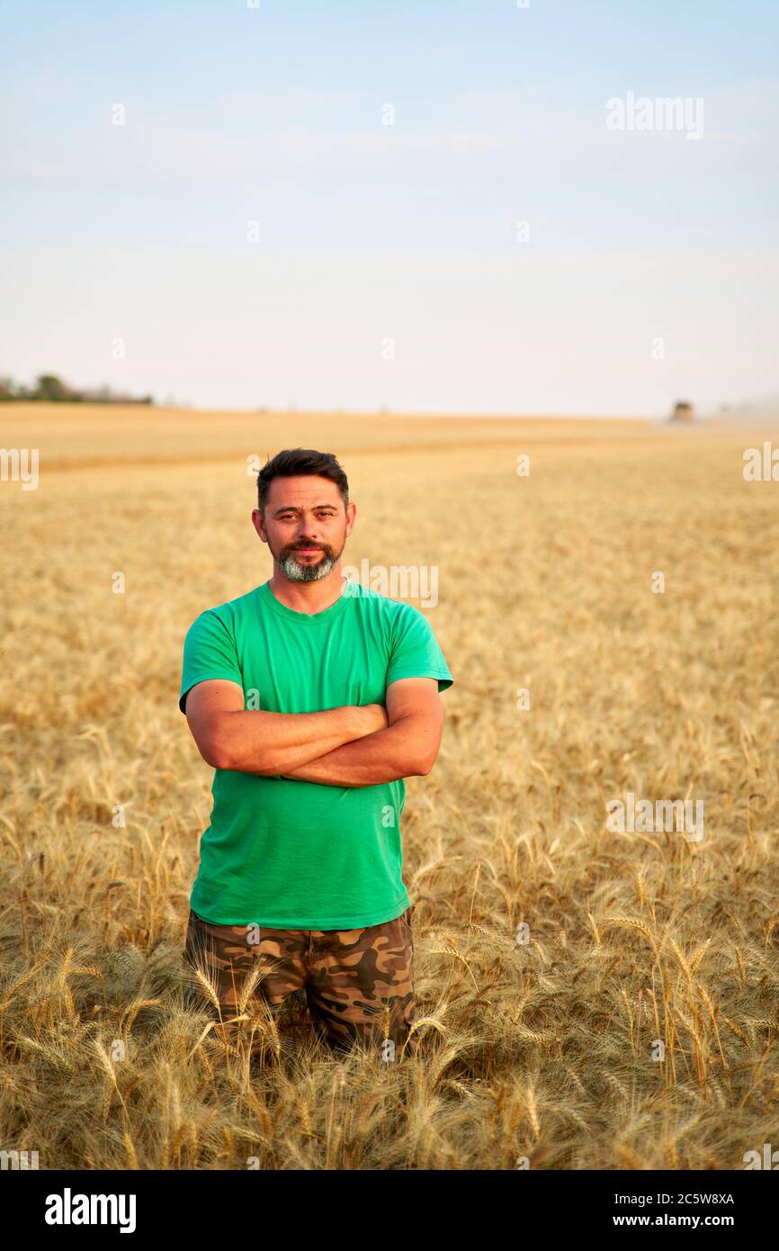 Happy farmer proudly standing in wheat field with arms crossed on chest ...