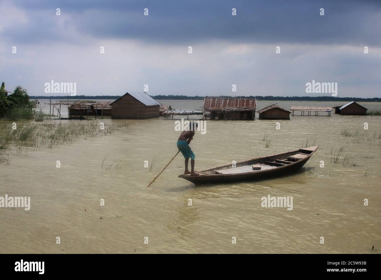A kid rows a boat on a flooded area in Tangail.Around 129,000 villagers are marooned in and 3,686 hectares of croplands have been remaining submerged in Tangail due to floods. Stock Photo