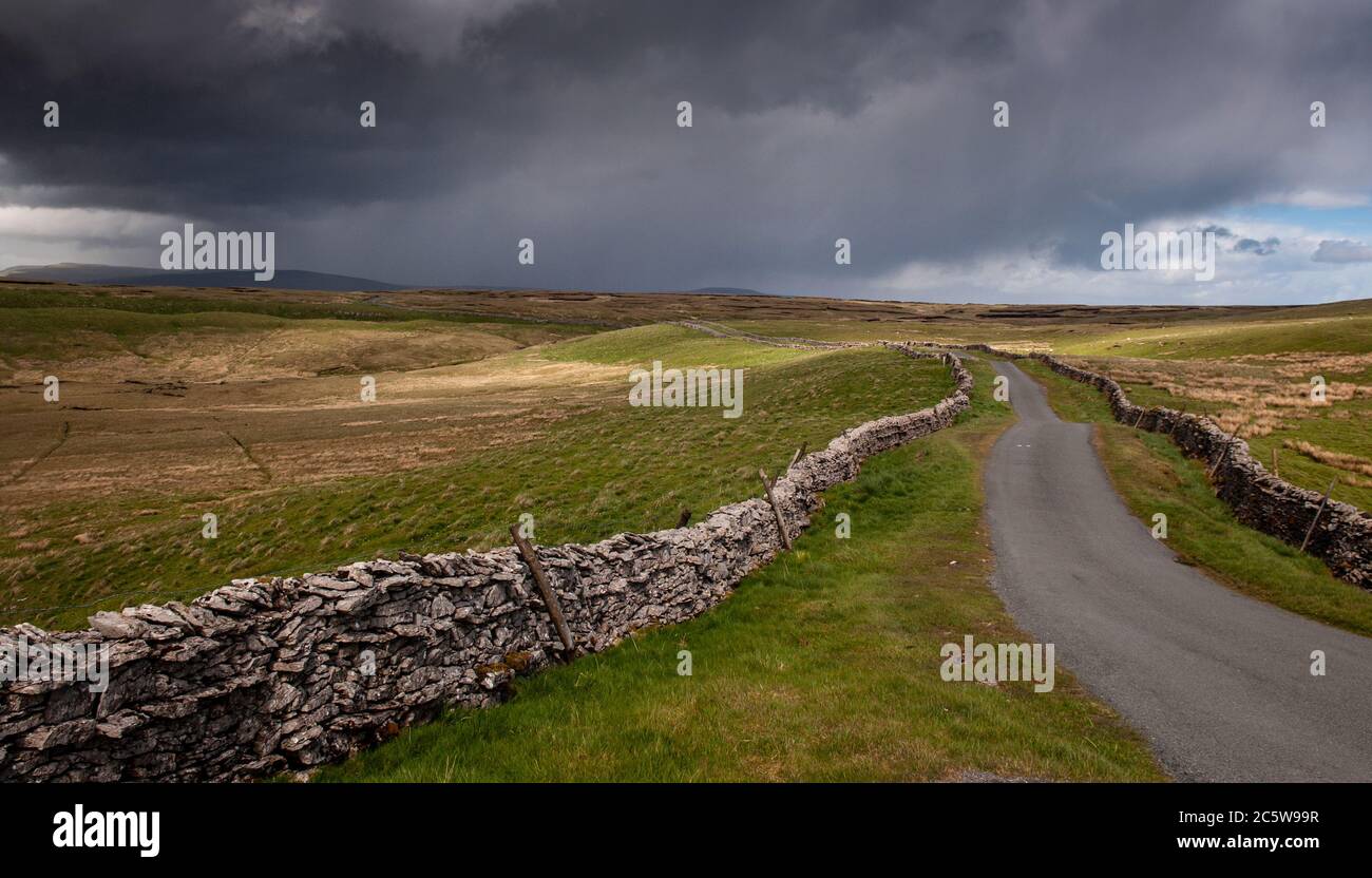 A country lane winds between drystone walls over the sheep pasture moorland hills at Cowgill Head above Garsdale and Dentdale in England's Yorkshire D Stock Photo