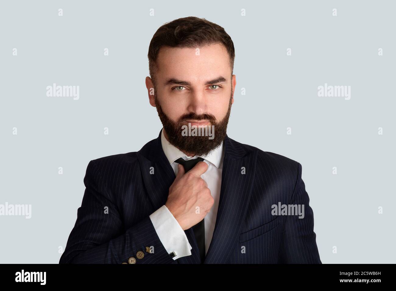 Handsome gentleman in business suit adjusting his tie against grey ...