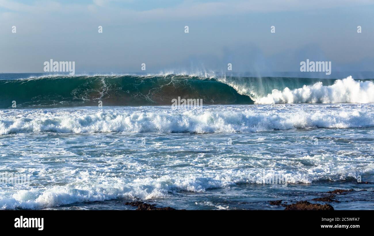 Ocean wave upright wall of blue and white water crashing on shallow reef sandbars . Stock Photo