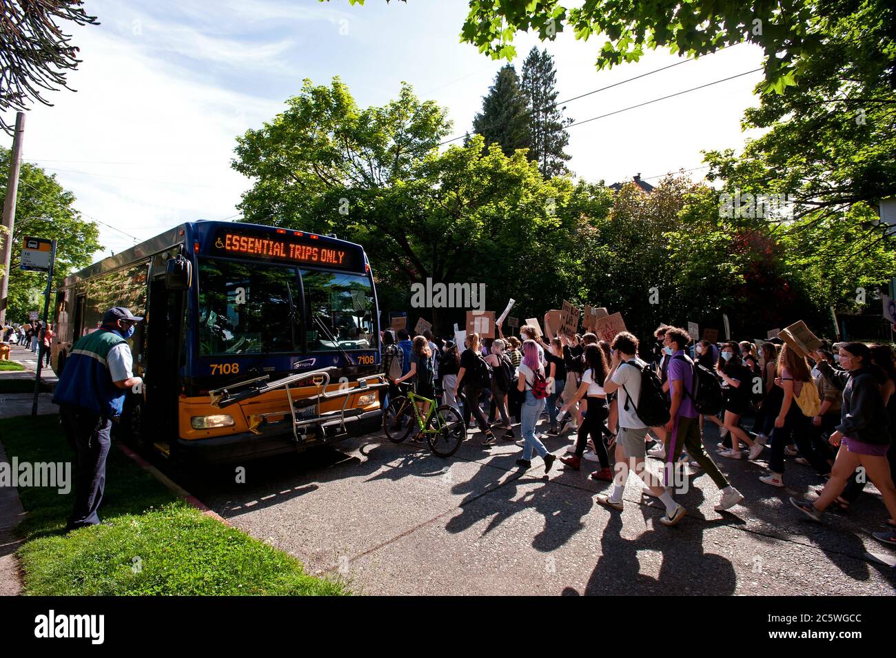 Seattle, Washington State. Student-led protest passing by city bus with 'Essential Trips Only' sign. Stock Photo