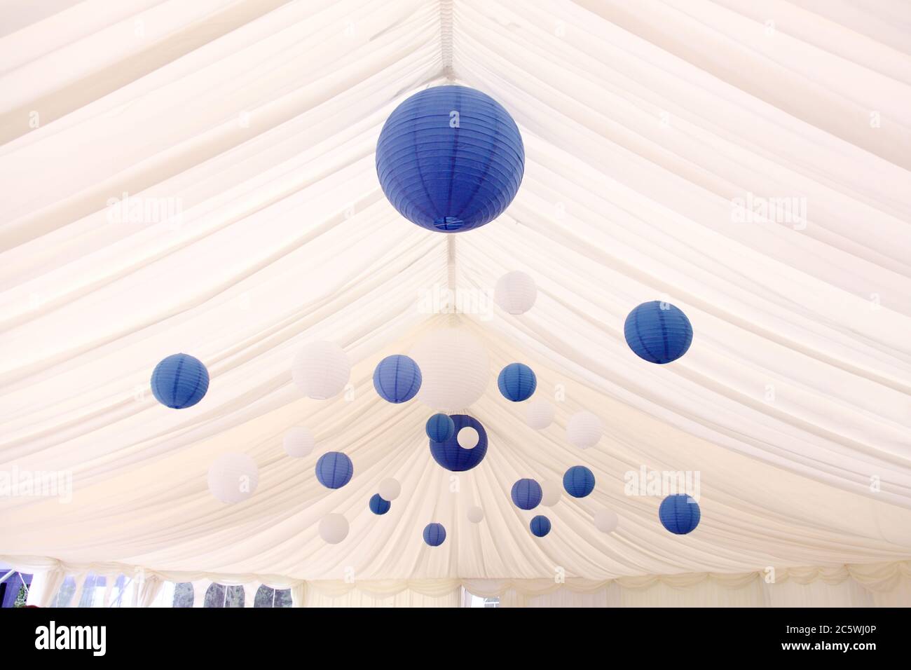 Blue & white wedding pom poms or Chinese paper lanterns in a white wedding marquee as wedding venue decorations. Stock Photo