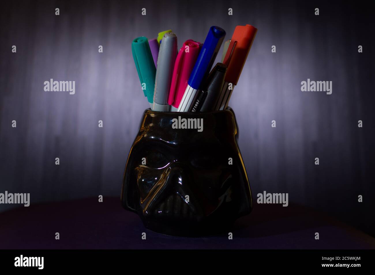 Black pencil holder with colored markers and dark background Stock