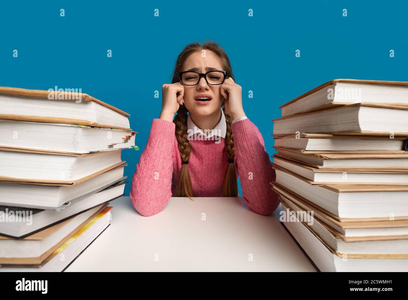 Overwork concept. Girl among books is crying Stock Photo