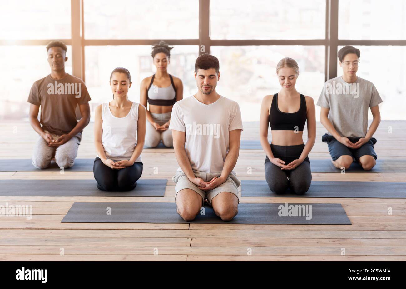 Group Meditation. Multiethnic People Practicing Breathing Yoga Exercises With Instructor In Studio Stock Photo
