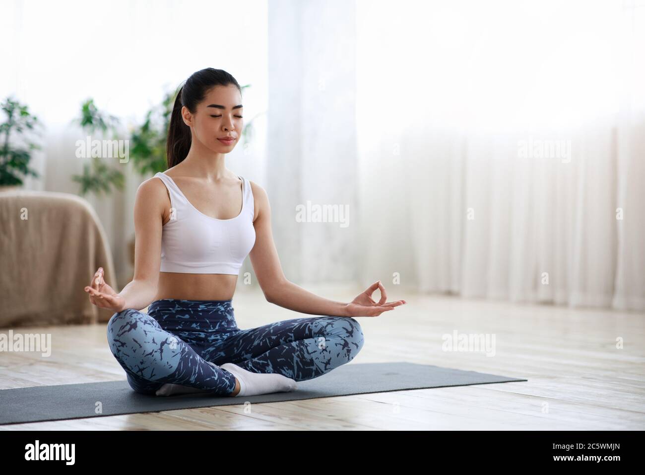 Life Harmony. Calm Asian Girl Meditating In Lotus Position At Home Stock Photo