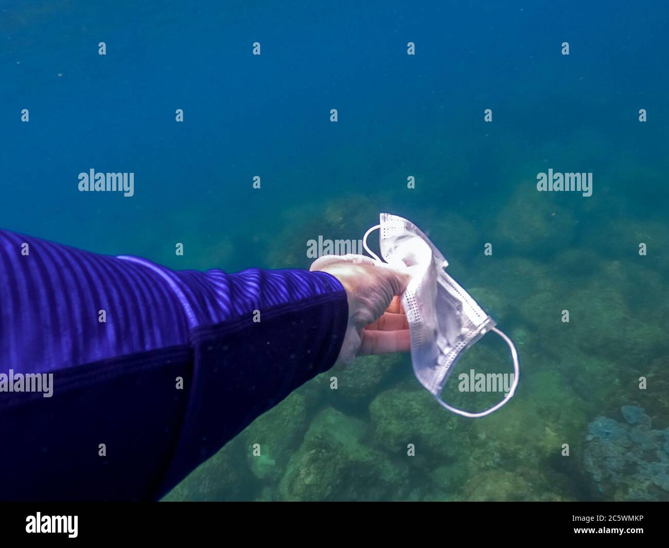 Close up of man hand picking up mask for cleaning area in dirty ocean. Snorkeler diving underwater and cleaning up the sea. Environmental and coast pl Stock Photo