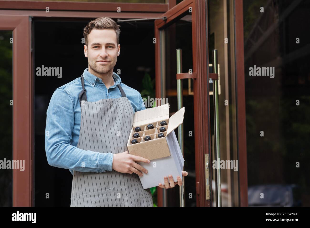 Barman in apron holds box with bottles at entrance to bar Stock Photo