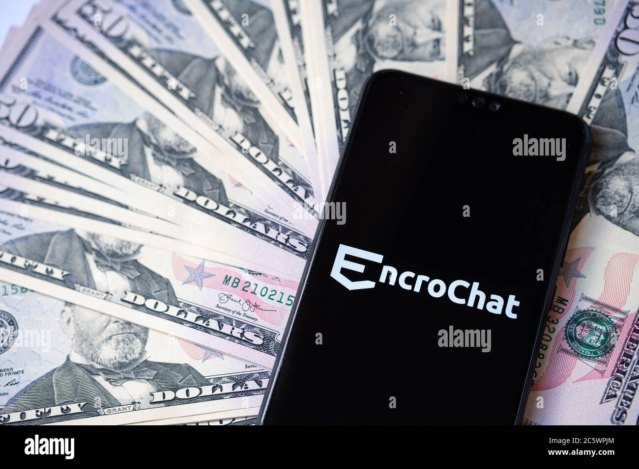 Stone / UK - July 5 2020: EncroChat logo on the smartphone and spread pile of dollars. Selective focus. Stock Photo