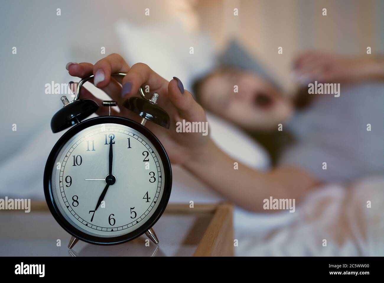 Close up sleepy teenager girl turning alarm off in the morning while