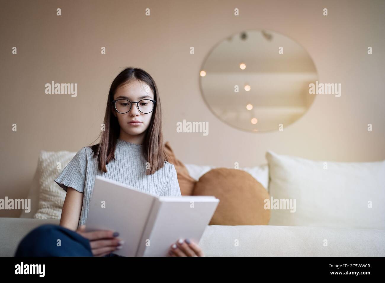 Pretty teenage girl reading book at home while sitting on sofa Stock Photo