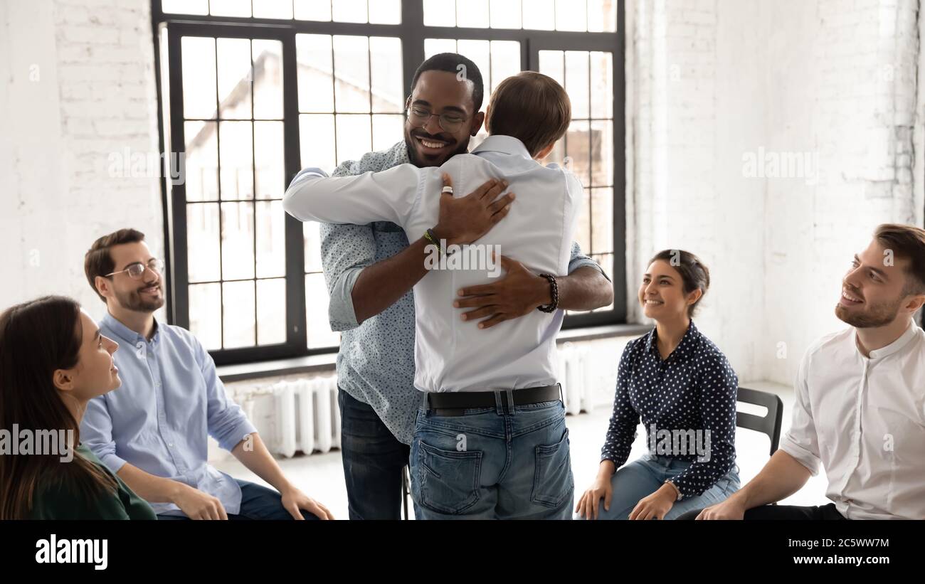 African and Caucasian men embracing during group therapy counseling session Stock Photo