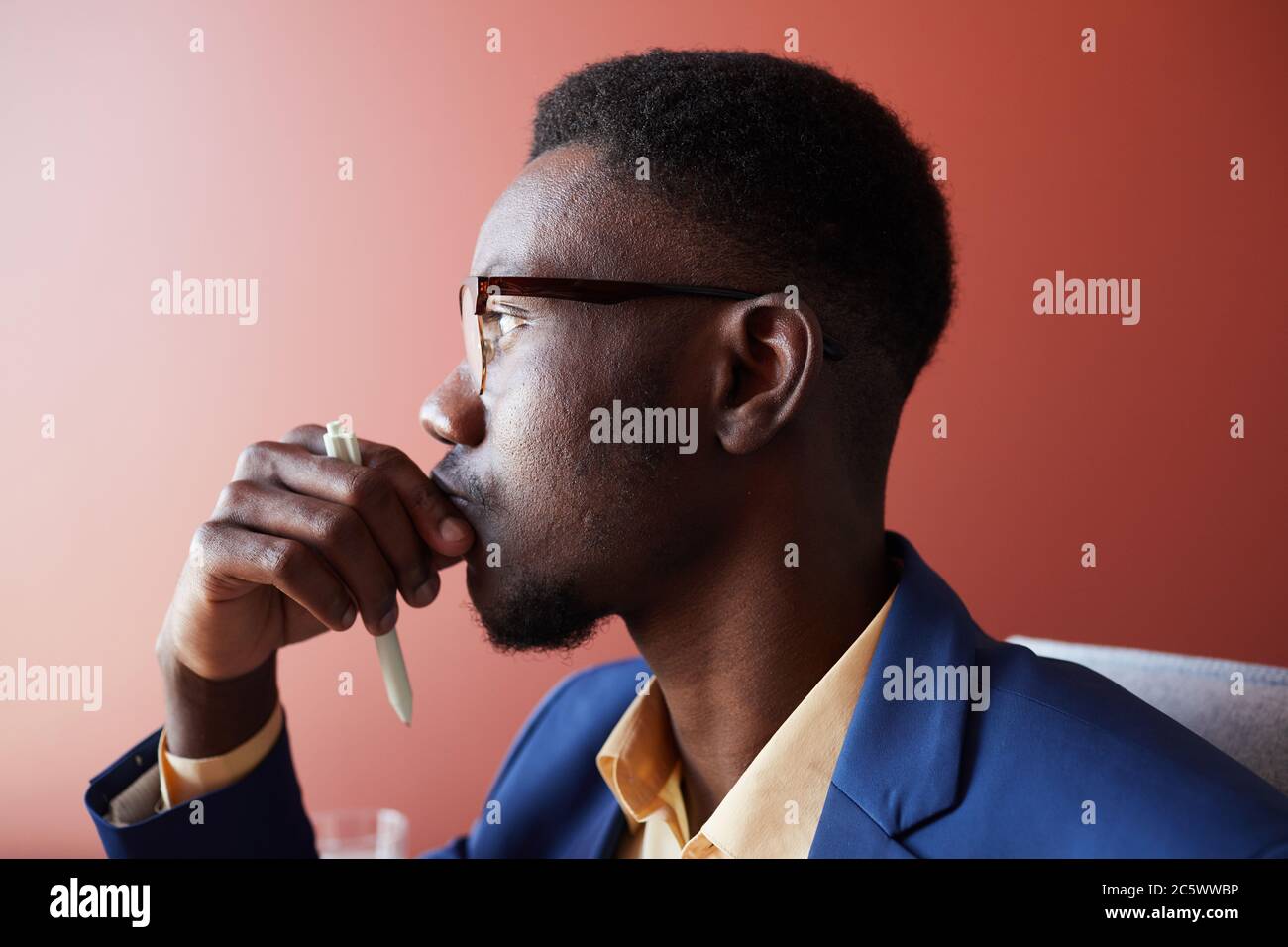 Side view portrait of young African-American businessman thinking while working in office against red wall, copy space Stock Photo