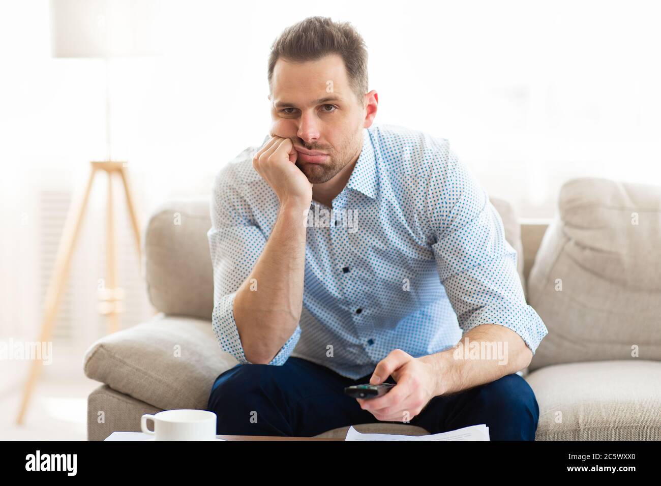 Bored man watching TV at home, holding remote control Stock Photo