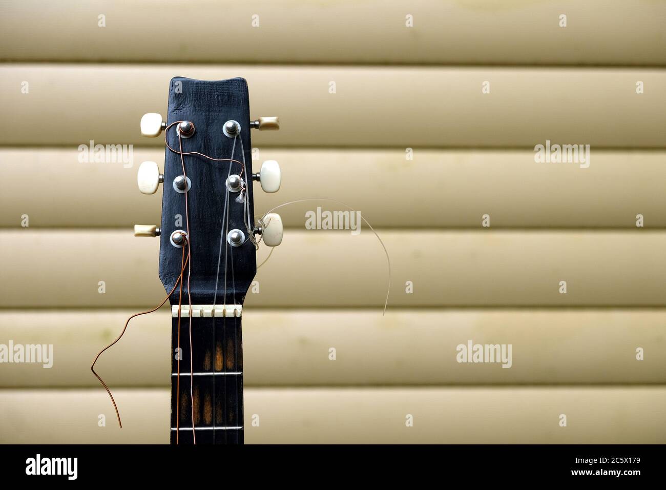 Guitar neck and head in bad condition with broken strings in front of house wall front view close up Stock Photo