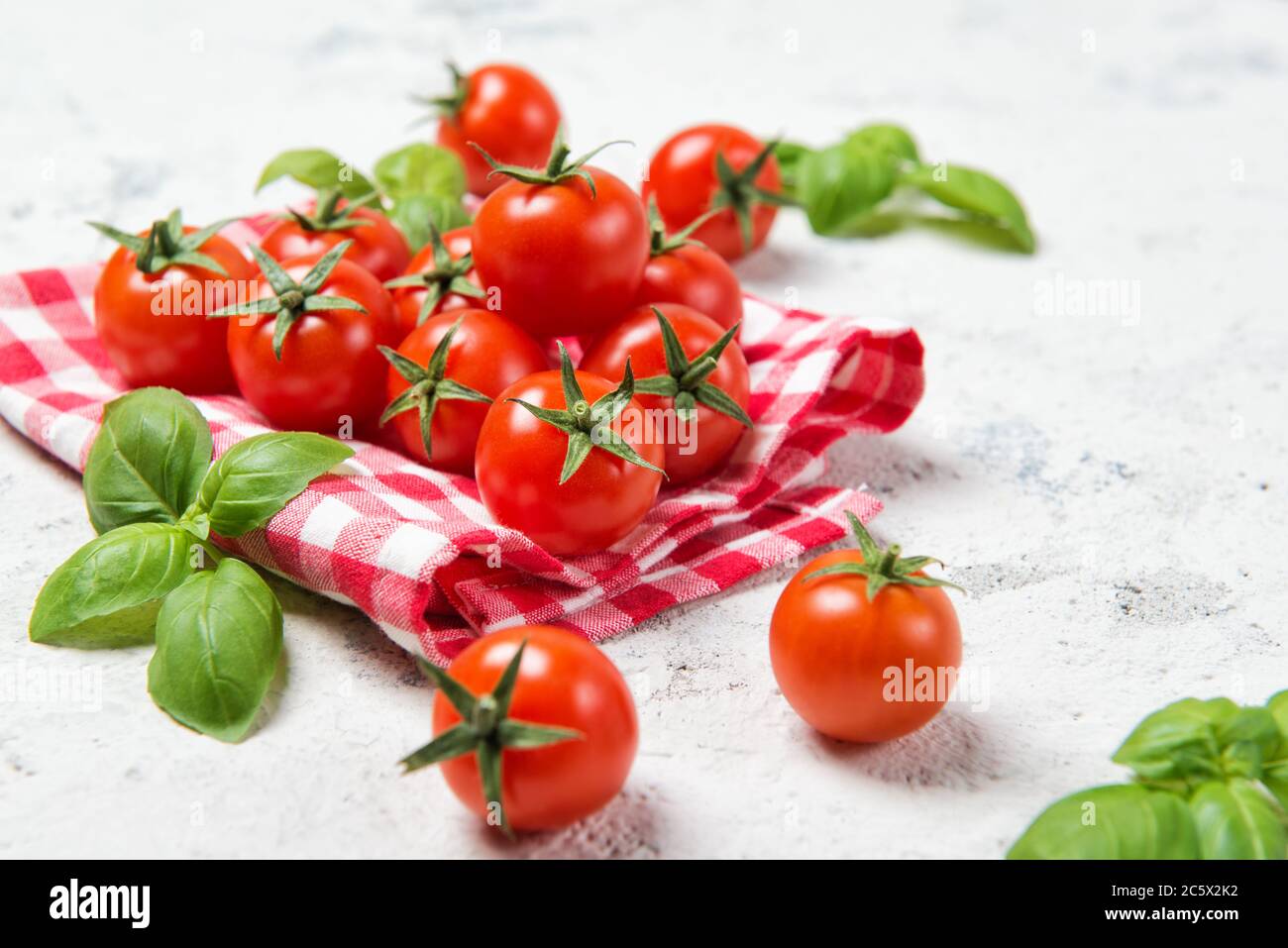 Fresh cherry tomatoes with basil leaves on a stone table with red ...