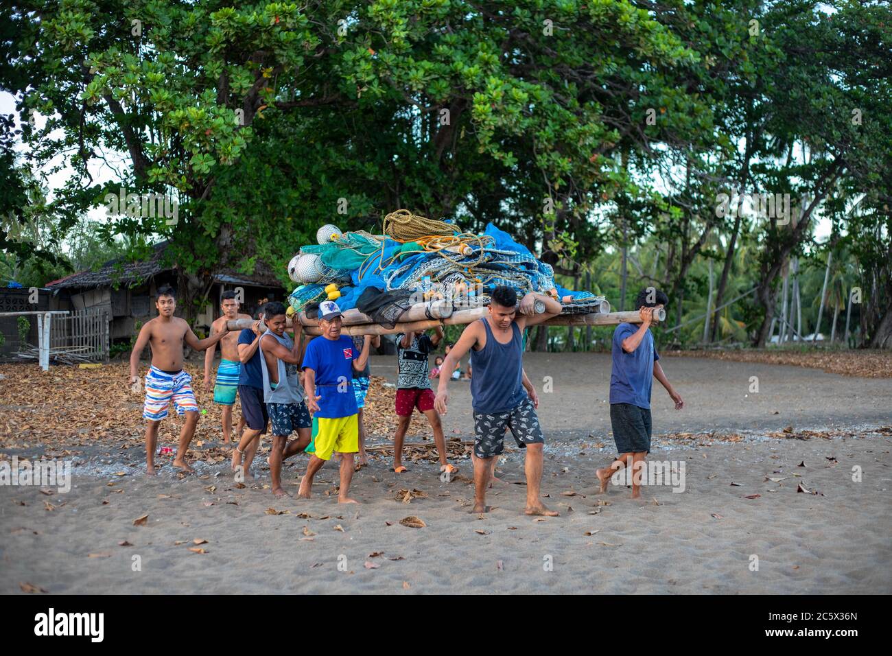 Dumaguete, Philippines - 23 Mar 2020: local fishermen preparing for night fishing. Filipino men carrying bunch of fishing net on beach. Onshore fishin Stock Photo