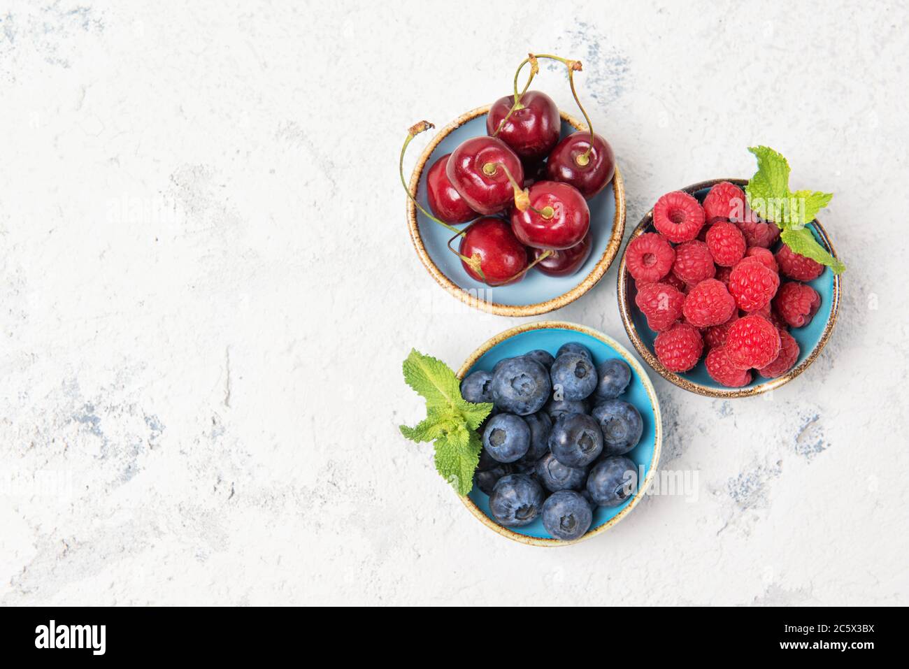 Assorted fresh juicy berries. Cherry, blueberry and raspberry in bowls, top view Stock Photo