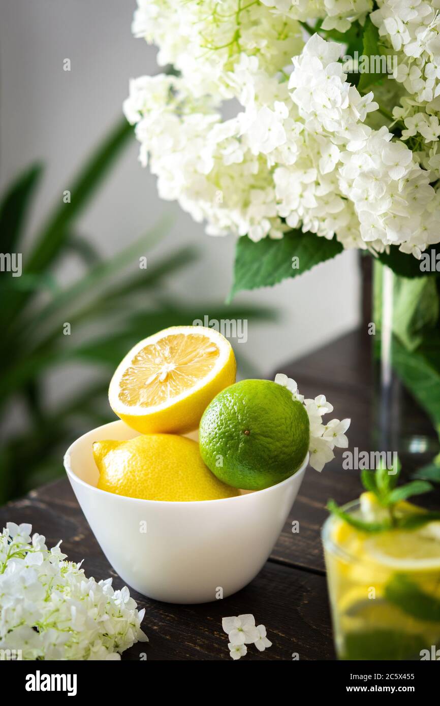 Vase of flowers viburnum opulus Roseum and plate with lemons and lime, refreshing lemonade with ice Stock Photo