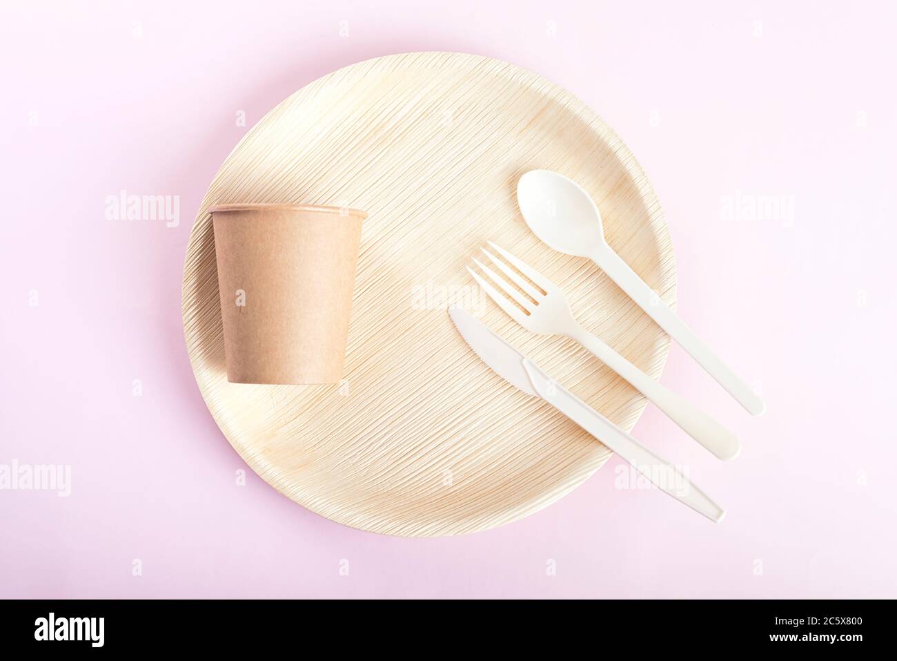 Set of disposable plate, cup, spoon, fork, knife on light pink background. Stock Photo
