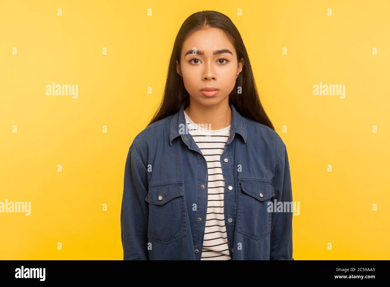 Portrait of serious unsmiling brunette girl in denim shirt standing calm, looking focused concentrated at camera, earnest attentive expression. indoor Stock Photo