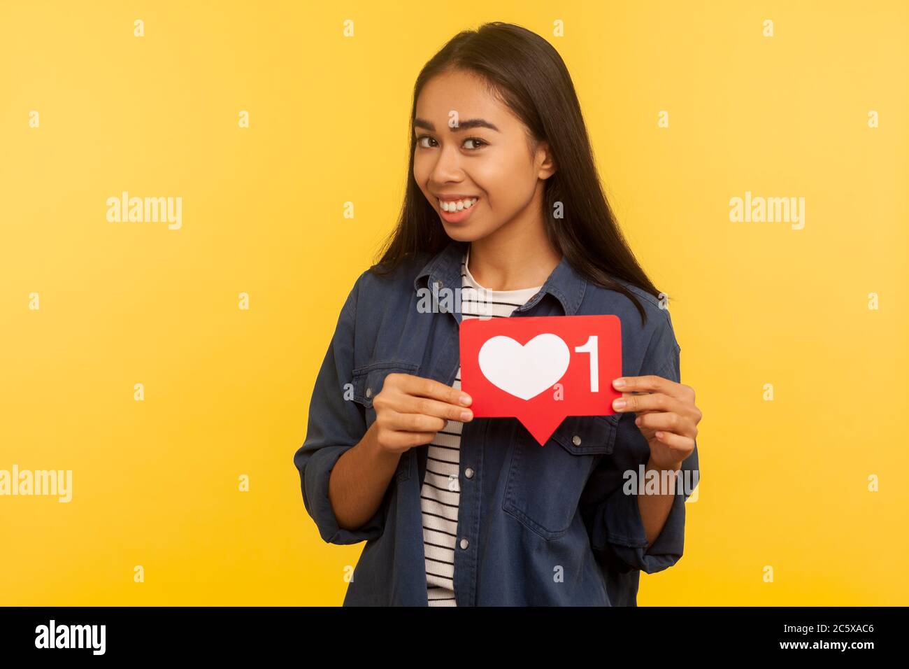 Portrait of playful girl in denim shirt showing heart Like icon ...