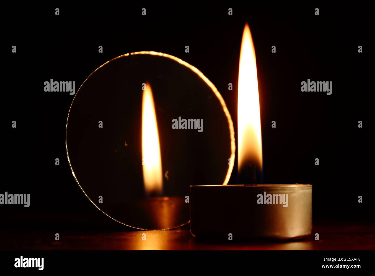 burning candle next to a mirror showing its reflection, dark background Stock Photo