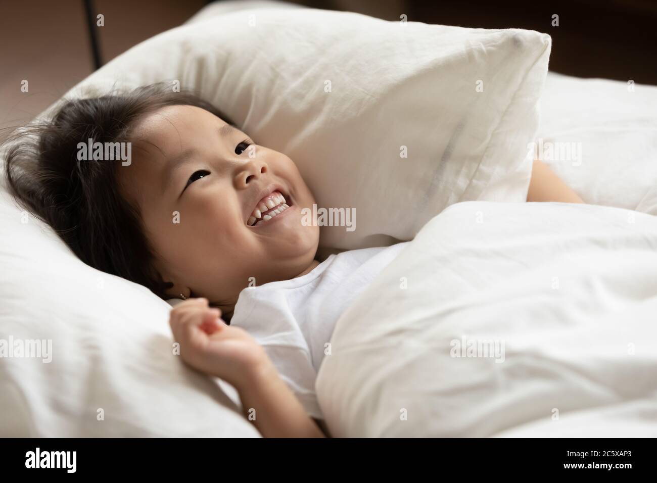 Smiling adorable little asian ethnic kid waking up in morning. Stock Photo