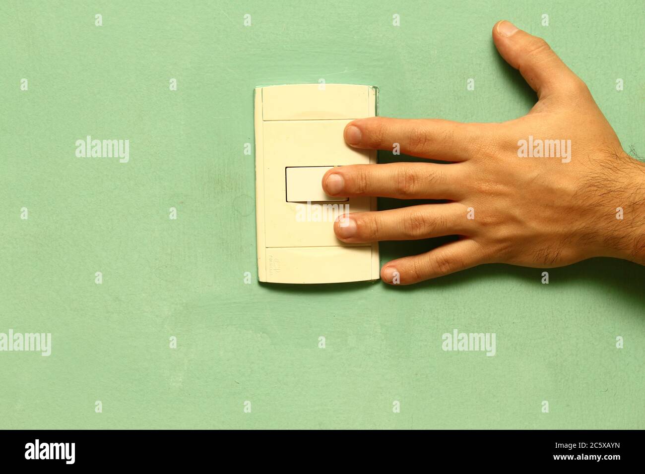 left hand touching a power switch on a green wall. Stock Photo